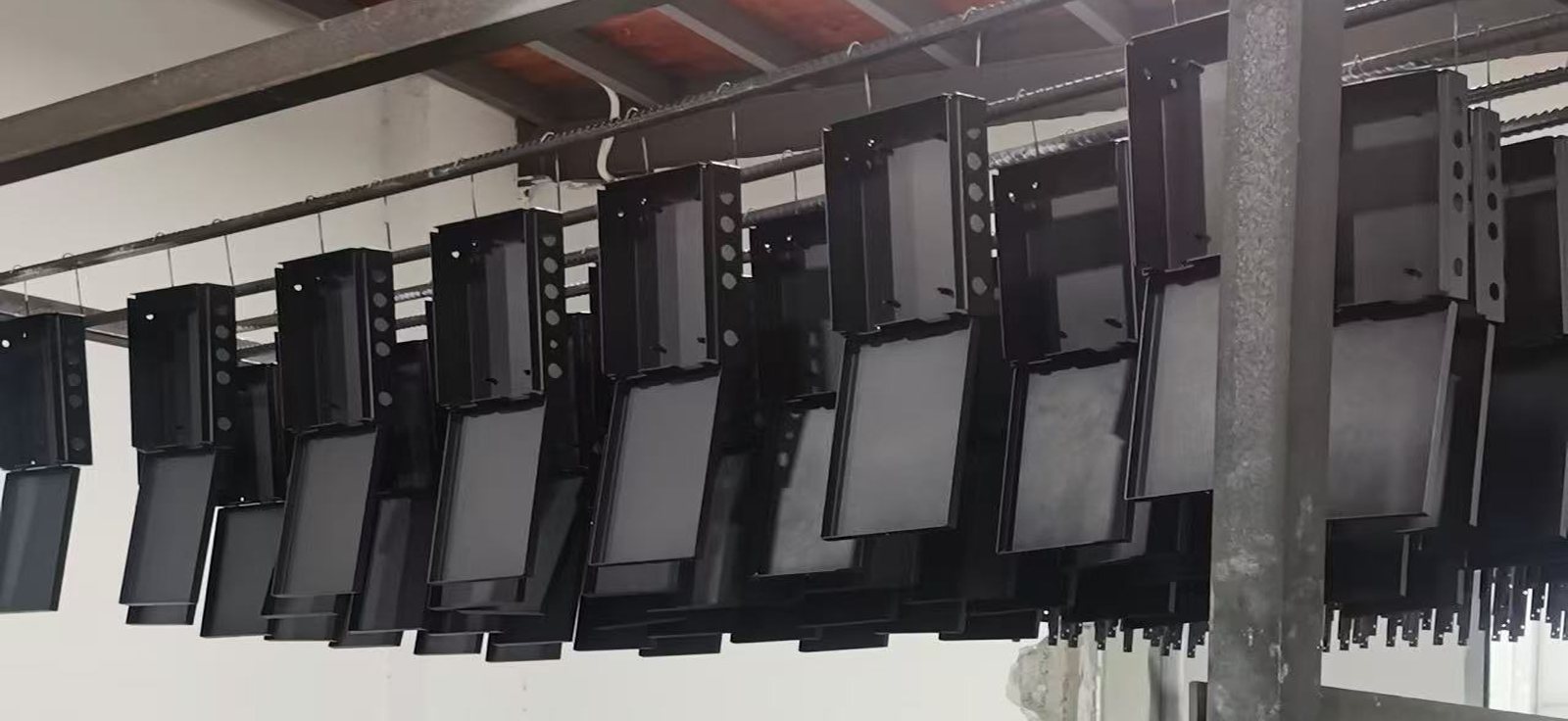 Powder-coated black sheet metal parts hanging on the paint line, awaiting inspection